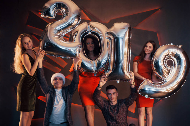 Nový rok 2019 se blíží. Skupina veselých mladých nadnárodních lidí v Santově klobouku se stříbrnými čísly a házení konfet na párty. Šťastný nový rok - Fotografie, Obrázek