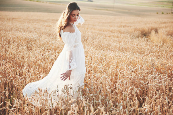 Happy young girl with long, beautiful hair standing in a wheat field under the sunlight. - Foto, afbeelding