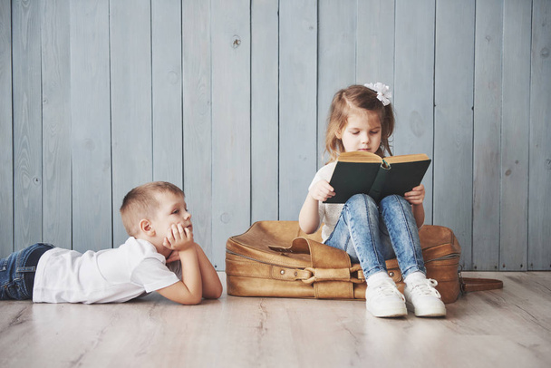 Ready to big travel. Happy little girl and boy reading interesting book carrying a big briefcase. Freedom and imagination concept. - Zdjęcie, obraz