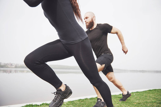 Couple jogging and running outdoors in park near the water. Young bearded man and woman exercising together in morning. - Foto, imagen