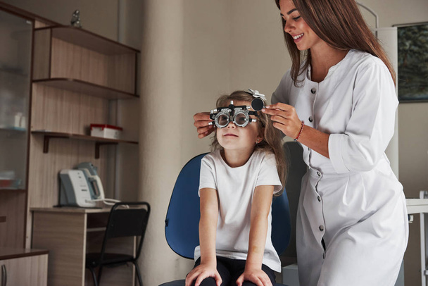 Work in progress. Little girl in glasses sitting in clinic and having her eyes tested. - Φωτογραφία, εικόνα