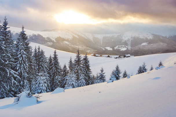 Majestueuze zonsondergang bij een klein dorp op een besneeuwde heuvel onder Oekraïense. Dorpen in de bergen in de winter. Prachtig winterlandschap. Karpaten, Oekraïne, Europa. - Foto, afbeelding