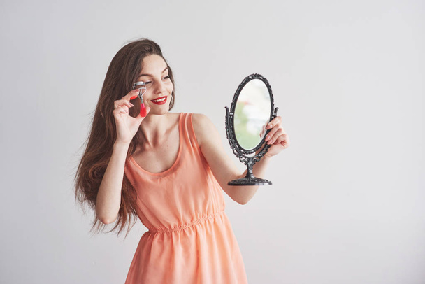 Young beautiful woman holding a mirror and looking at the brows tool. - Foto, immagini