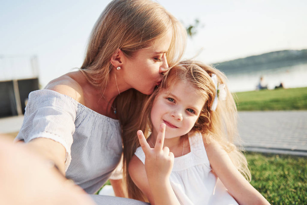 Happy young mother with a playful daughter in a park near the water. - 写真・画像