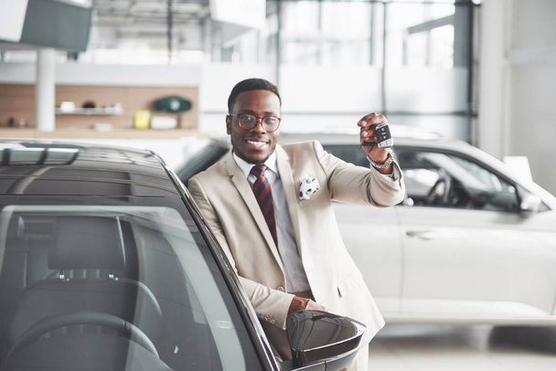 Handsome black man in dealership is hugging his new car and smiling. - Foto, Bild