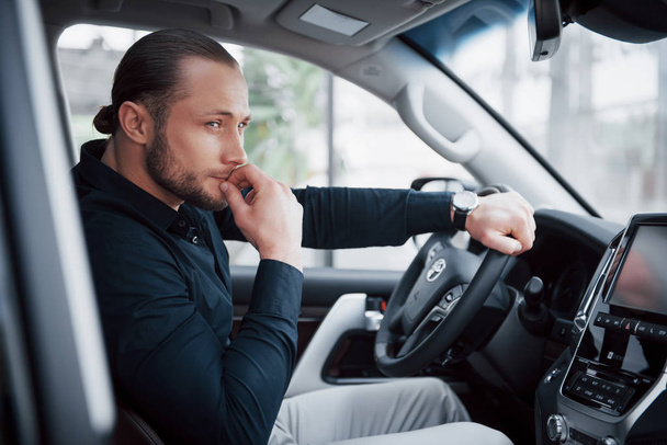 Αυτοπεποίθηση νεαρός επιχειρηματίας κάθεται στο τιμόνι του νέου του αυτοκινήτου. - Φωτογραφία, εικόνα