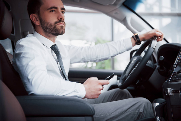 Satisfeito jovem homem de negócios olhando para o telefone celular enquanto dirige um carro
. - Foto, Imagem