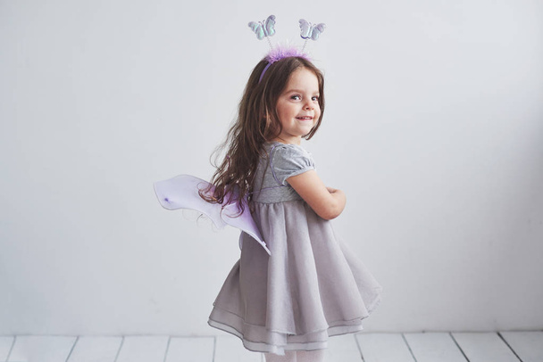 Cheerful mood and sincenery smile. Lovely little girl in fairy costume standing in room with white background. - 写真・画像