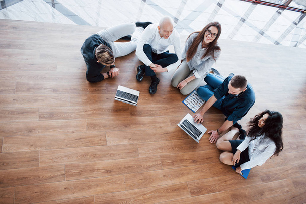 Young creative people in modern office. Group of young business people are working together with laptop. Freelancers sitting on the floor. Cooperation corporate achievement. Teamwork concept. - Fotografie, Obrázek