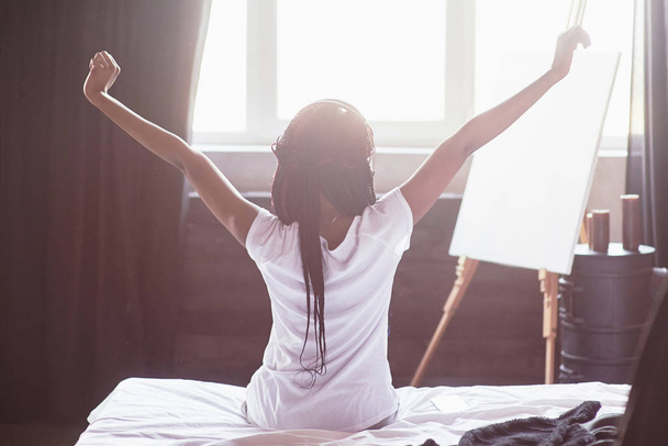 Beautiful black woman waking up in her bed, she is smiling and stretching. - Photo, Image