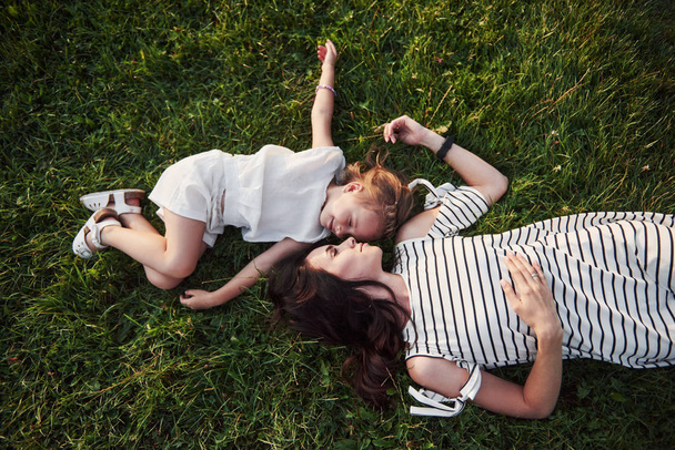 boldog kis lány és az anyja, szórakozás kint a zöld fű a napsütéses nyári napon - Fotó, kép