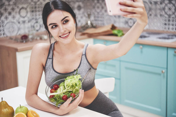 Young woman eating healthy salad with cherry tomatoes in the kitchen after a fitness session. - Photo, image
