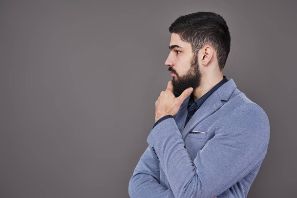 Portrait in profile of freelancer man with beard in jacket standing against gray backdrop. - Zdjęcie, obraz