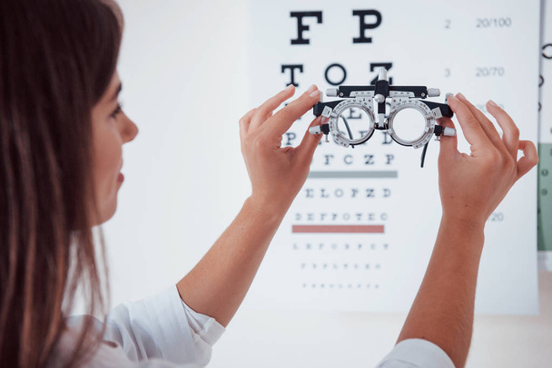 Phoropter is on the front of girl. Photo from behind. Woman looking through the glasses eye chart. - Foto, imagen