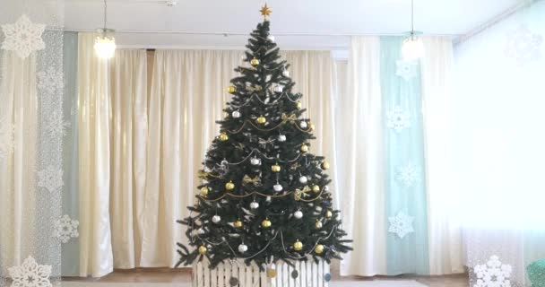 Λευκό δωμάτιο με εσωτερική διακόσμηση Χριστουγέννων και Πρωτοχρονιάς. Πράσινο δέντρο διακοσμημένο με παιχνίδια και αναβοσβήνει γιρλάντα - Πλάνα, βίντεο