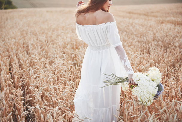 Beautiful girl in white dress running on the autumn field of wheat at sunset time - Фото, изображение