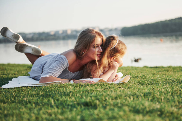 Attractive happy young mother lying with her cute daughter on the grass in the park - Fotoğraf, Görsel
