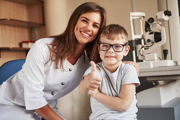 Female eye doctor sitting with the kid after doing the vision test. - Foto, Bild