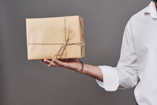Man's hands gives parcel wrapped in brown paper and tied with rough twine. - Photo, image