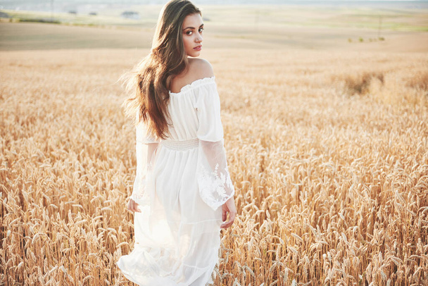 Happy young girl with long, beautiful hair standing in a wheat field under the sunlight. - Valokuva, kuva