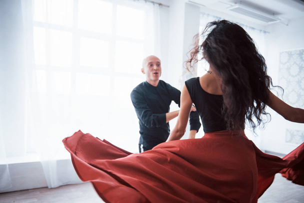 This is the art. Young pretty woman in red and black clothes dancing with bald guy in the white room. - Foto, Bild