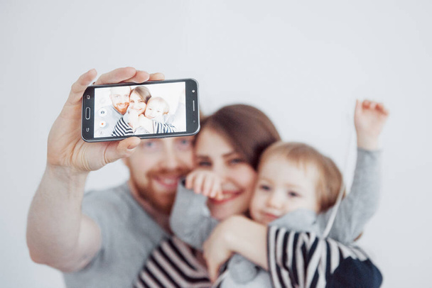 family, holidays, technology and people - smiling mother, father and little girl making selfie with camera over white background. - Foto, imagen