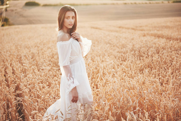 Счастливая молодая девушка с длинными, красивыми волосами, стоящая на пшеничном поле под солнцем
. - Фото, изображение