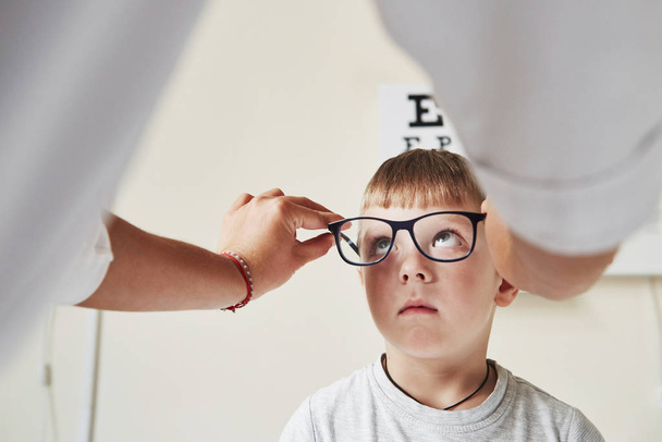 Boy looking at the specs. Doctor giving the child new black glasses for his vision. - 写真・画像