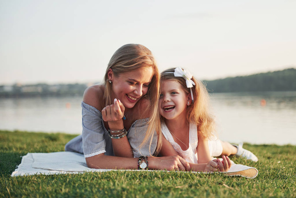 Attractive happy young mother lying with her cute daughter on the grass in the park - Foto, Bild