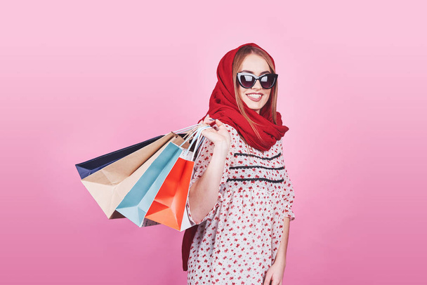 Portrait of young happy smiling woman with shopping bags on the pink Background. - Foto, afbeelding