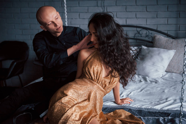 Gentle touching. Couple in classic wear sits in front of the beautiful luxury decorated bed. - Valokuva, kuva