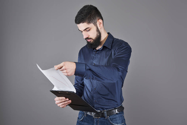 Concentrated young attractive businessman in blue shirt planning and writing in clipboard. - Photo, image