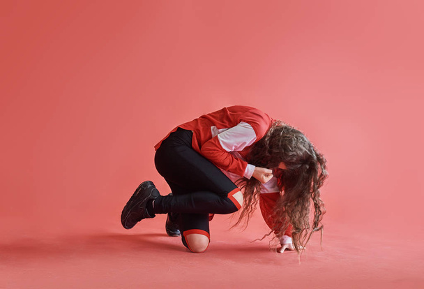 Young beautiful cute girl dancing on red background, modern slim hip-hop style teenage girl jumping. - Foto, afbeelding