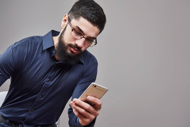 Happy man in glasses typing sms on gray background. - Fotografie, Obrázek
