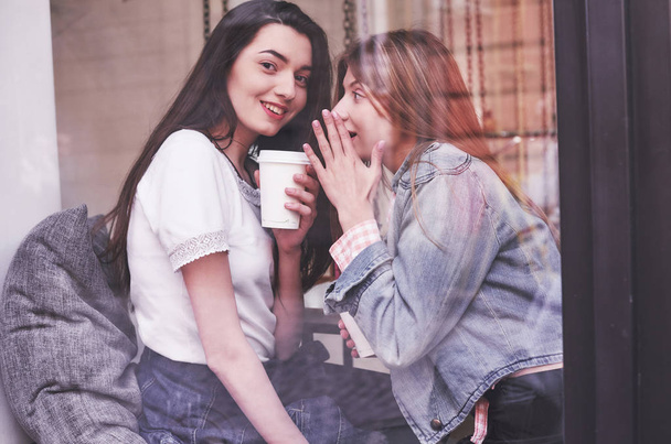 Δύο όμορφες νεαρές γυναίκες κάθονται σε ένα καφέ, πίνοντας καφέ και έχοντας μια ευχάριστη συζήτηση μετά τα ψώνια. - Φωτογραφία, εικόνα