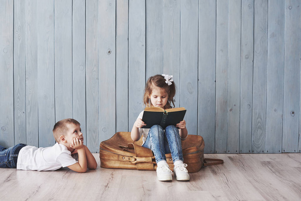 Ready to big travel. Happy little girl and boy reading interesting book carrying a big briefcase and smiling. Travel, freedom and imagination concept. - Φωτογραφία, εικόνα