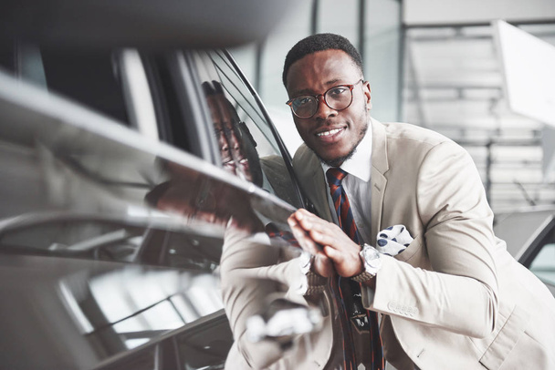 Handsome black man in dealership is hugging his new car and smiling. - Foto, imagen