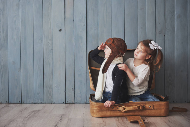 Happy kid in pilot hat and little girl playing with old suitcase. Childhood. Fantasy, imagination. Travel concept. - 写真・画像