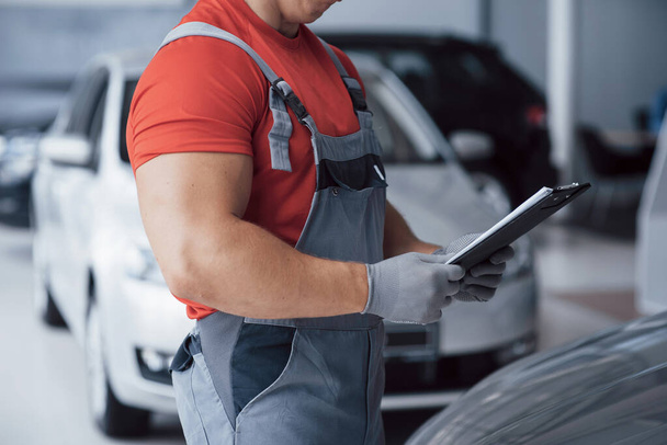 Handsome young auto mechanic in uniform is examining car in auto service. - Photo, image
