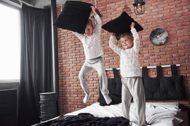 Naughty children Little boy and girl staged a pillow fight on the bed in the bedroom. They like that kind of game. - Photo, Image
