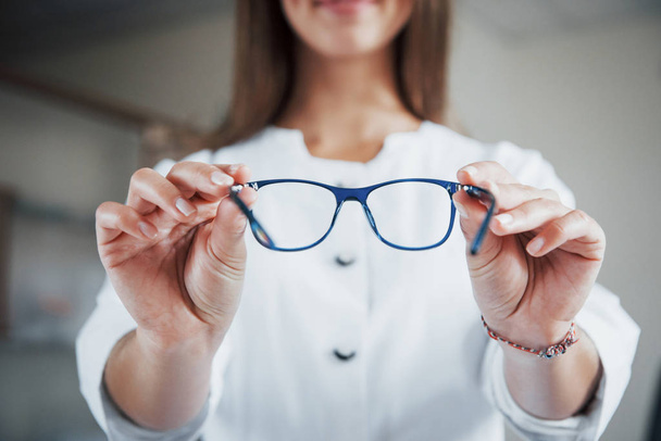 Front view. Female doctor showing the blue glasses by holding it in two hands. - Foto, afbeelding