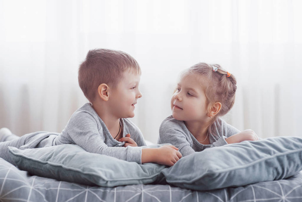 Kids playing in parents bed. Children wake up in sunny white bedroom. Boy and girl play in matching pajamas. Sleepwear and bedding for child and baby. Nursery interior for toddler kid. Family morning. - Foto, Imagem