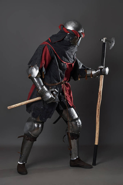 Medieval knight on grey background. Portrait of brutal dirty face warrior with chain mail armour red and black clothes and battle axe. - Foto, Imagem