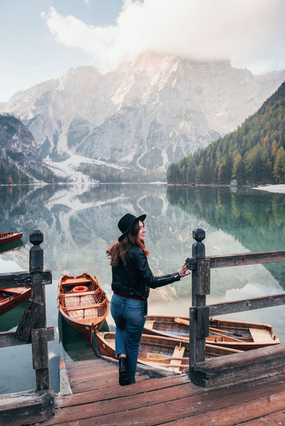 Great distance. Fog on the top of the hills. Woman in black hat enjoying majestic mountain landscape near the lake with boats. - Photo, image