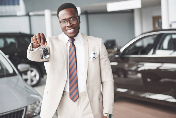 Young black businessman on auto salon background. Car sale and rent concept. - Фото, изображение