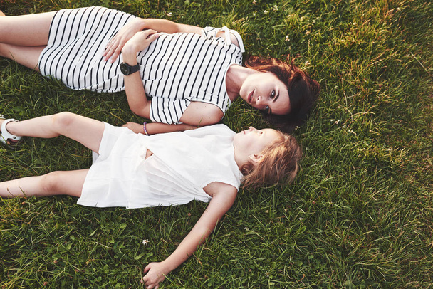Top view of children and mother laying down on the grass filled with sunshine and looking at each other. - Foto, Imagem