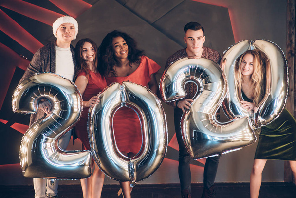 Wishing well. Group of beautiful young friends with inflatable numbers in hands celebrating new 2020 year. - Foto, imagen