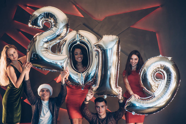 Divirtiéndose. Grupo de hermosos amigos jóvenes con números inflables en las manos celebrando el nuevo año 2019
. - Foto, Imagen