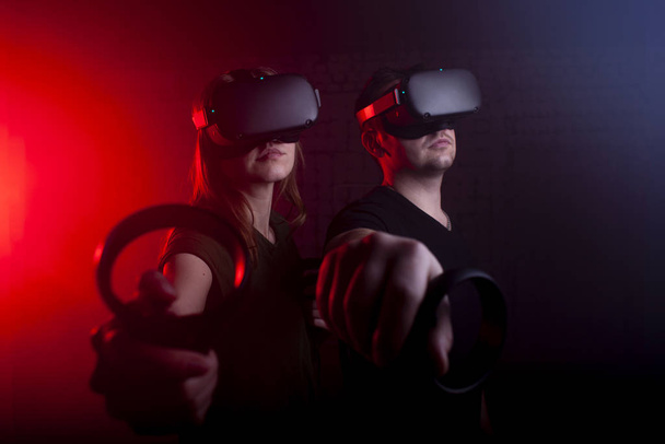 Paar Spieler in modernen drahtlosen Brillen der virtuellen Realität und Joysticks spielen einen Shooter im Spielzimmer, einen Mann und ein Mädchen in der virtuellen Welt - Foto, Bild