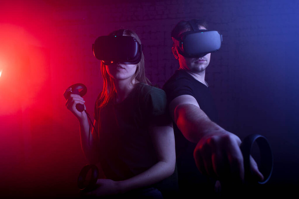 pair of gamers in modern wireless glasses of virtual reality and joysticks play a shooter in the game room, a guy and a girl in the virtual world - Photo, Image